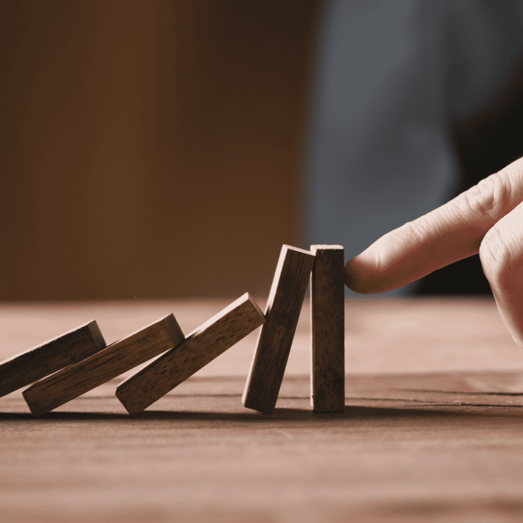 a set of standing dominoes that are falling against one another, and a finger holding up the last one to keep it from falling